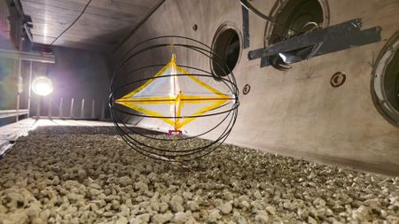 A round cage-like ball encloses a white diamond shape with a yellow outline that rolls over rocks in a dimly lit room.