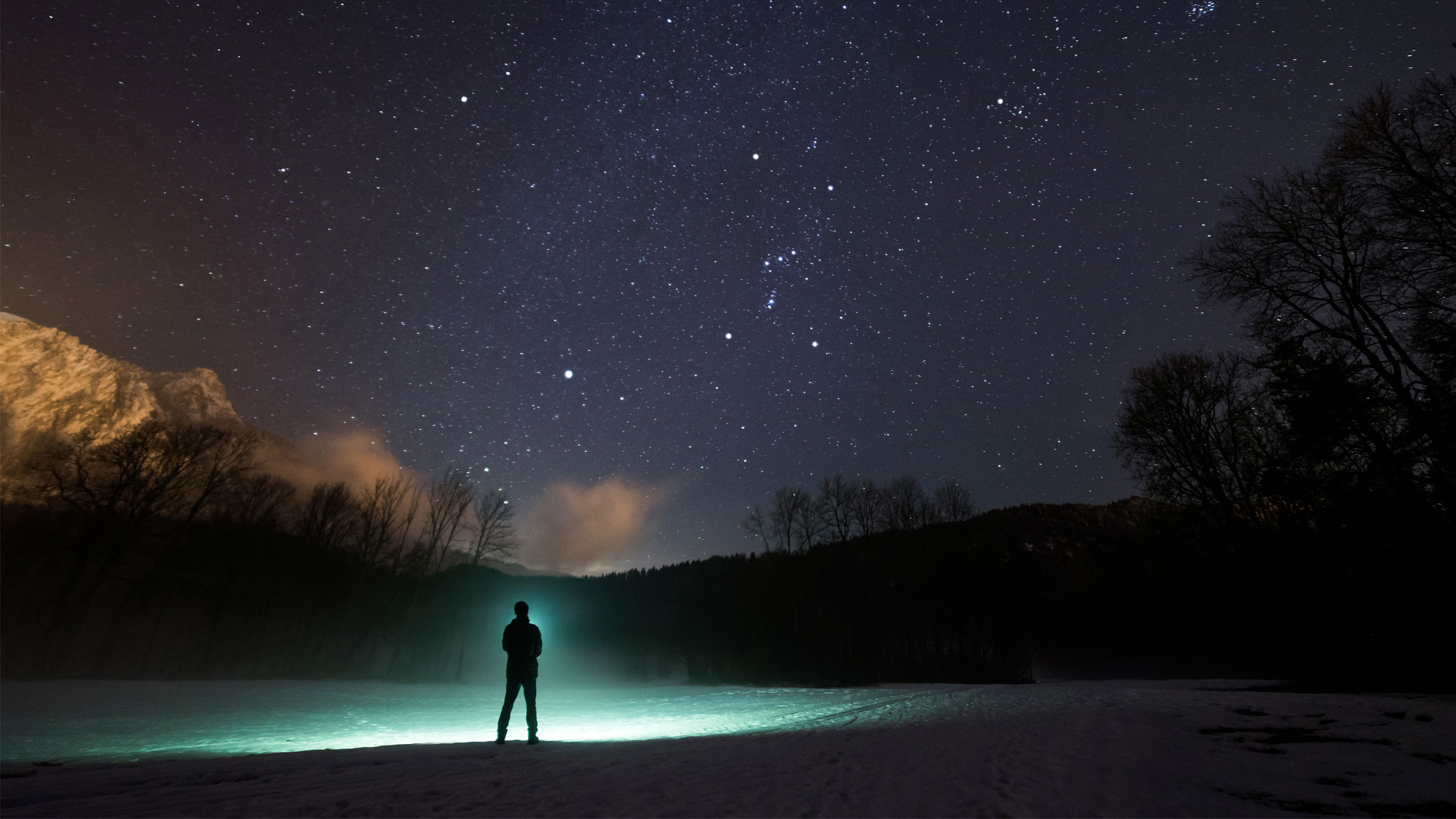 A person, with a glowing green outline, looking at the night sky with silhouetted hills.