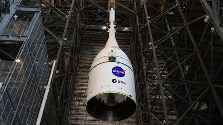 A white cone with NASA and ESA logos is lowered inside a large warehouse bay.