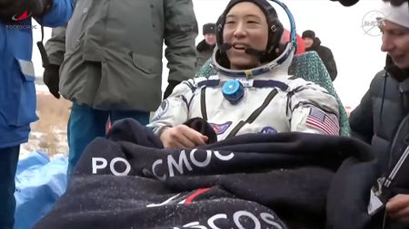 a man in a white pressure suit sits outside his spacecraft after landing back on Earth